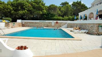 Una piscina con paredes de piedra, sillas de descanso y sombrillas.