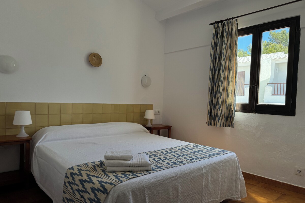 Hotellihuone, jossa on sänky, kaksi yöpöytää, ikkuna verhoilla ja näkymä ulos.