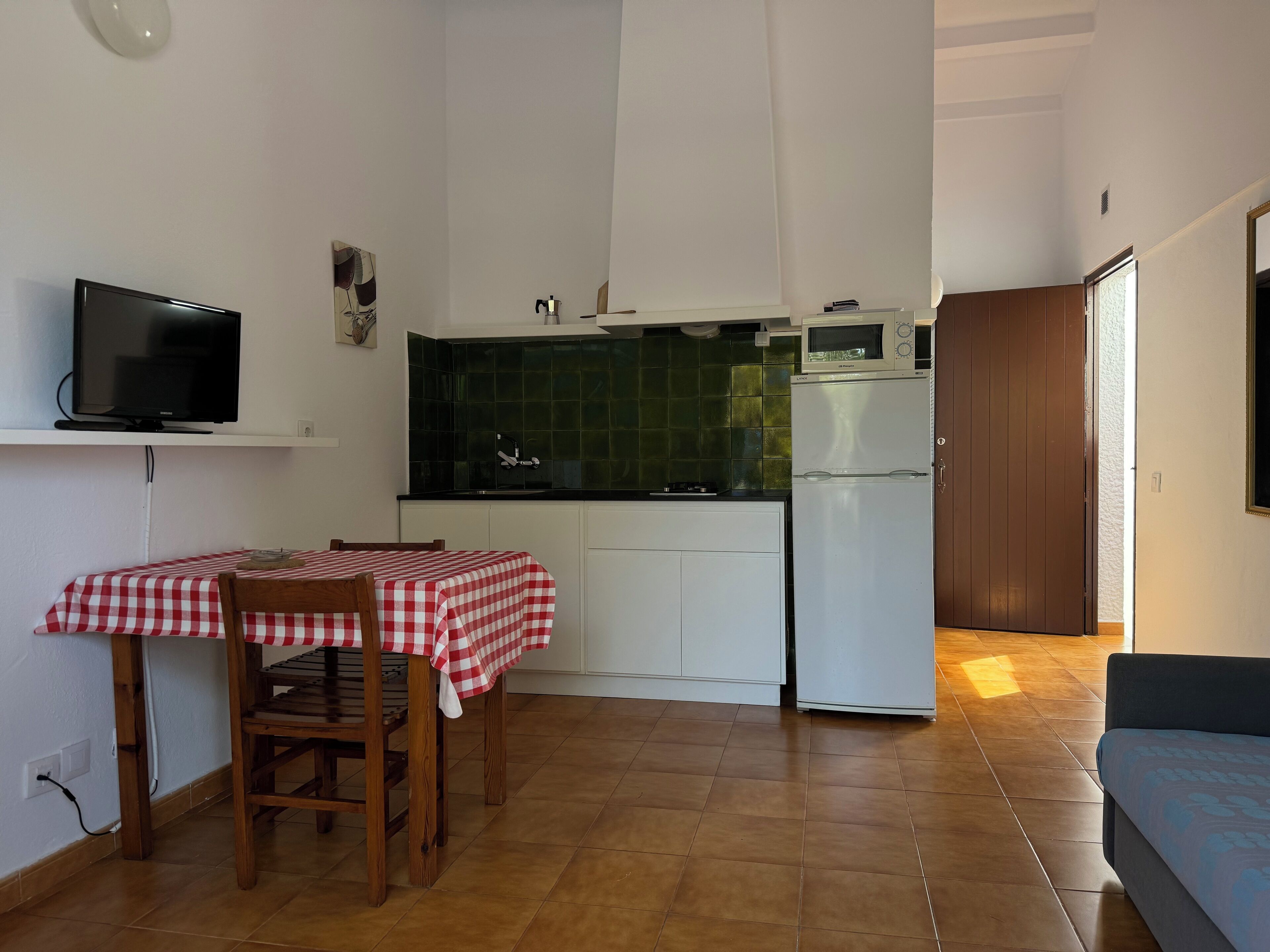 Cocina compacta con una mesa de comedor, televisor y refrigerador.