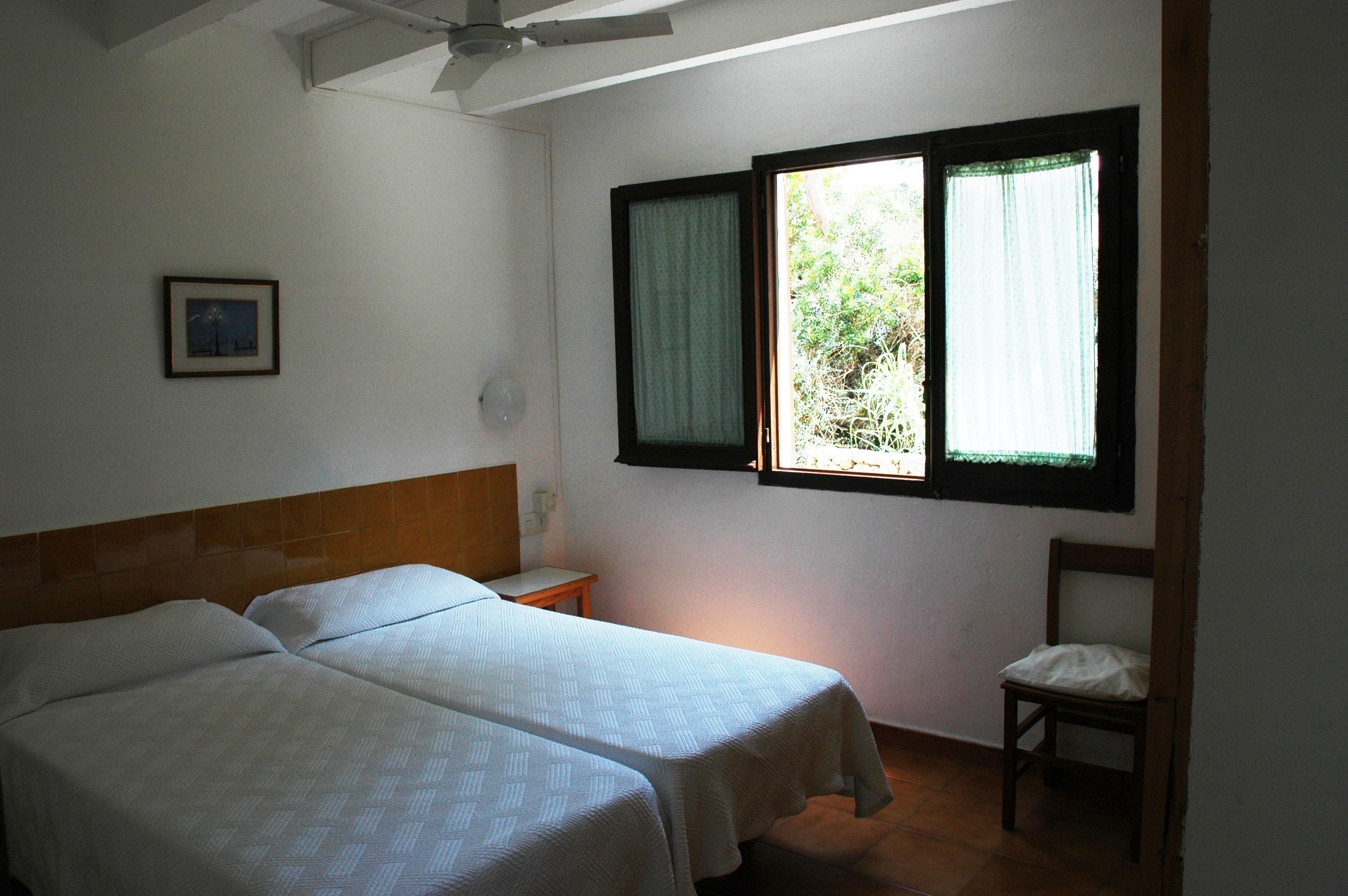 A room with two beds, a window with curtains, a chair, and a small table.