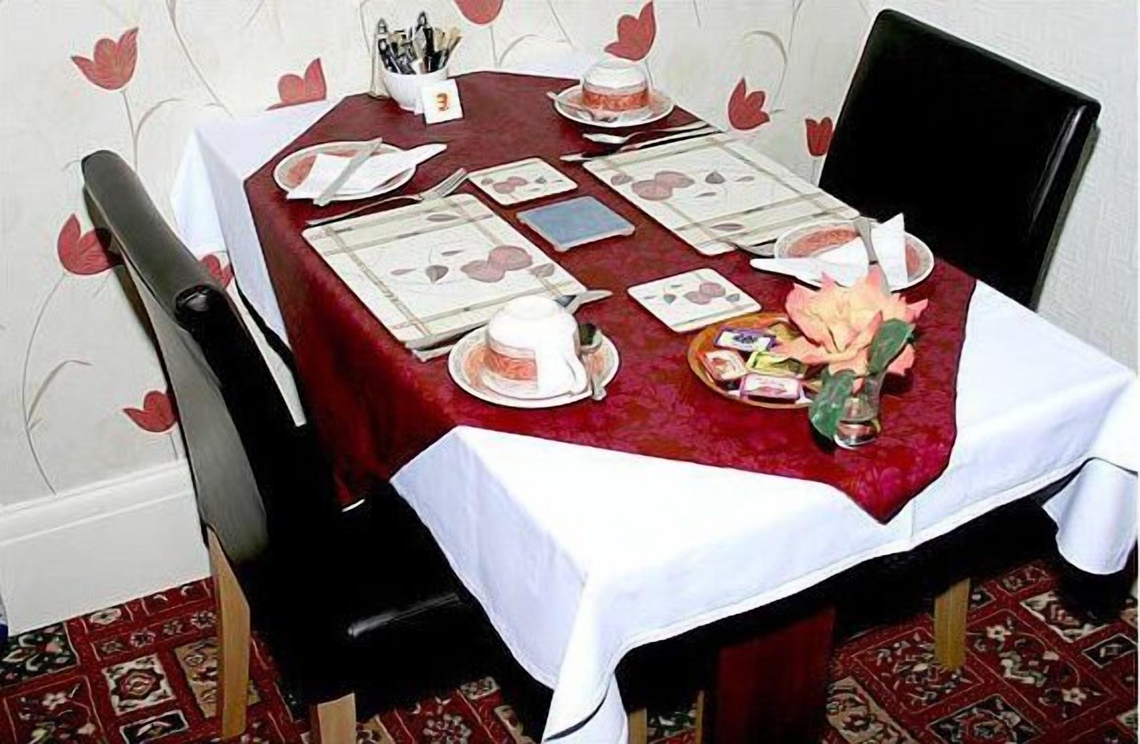 A dining table set with a red tablecloth, white napkins, and a floral centerpiece.