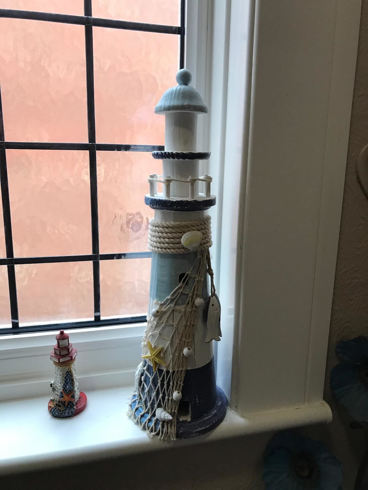 Una maqueta de faro sobre un alféizar con un patrón de cuadrícula y una pequeña figurita de faro.
