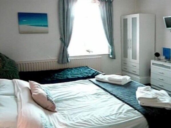 A bedroom with a bed, a wardrobe, a window with curtains, and a painting on the wall. - Lyndsay Guest House (Skegness)