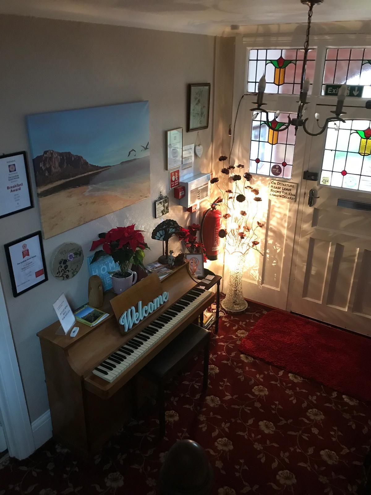 A cozy room with a piano, a painting, and a 'Welcome' sign.