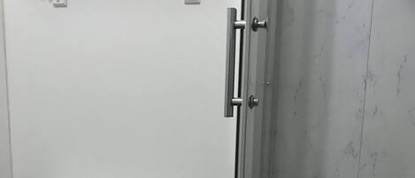 A bathroom with a toilet, a glass shower enclosure, and a shelf with toiletries.