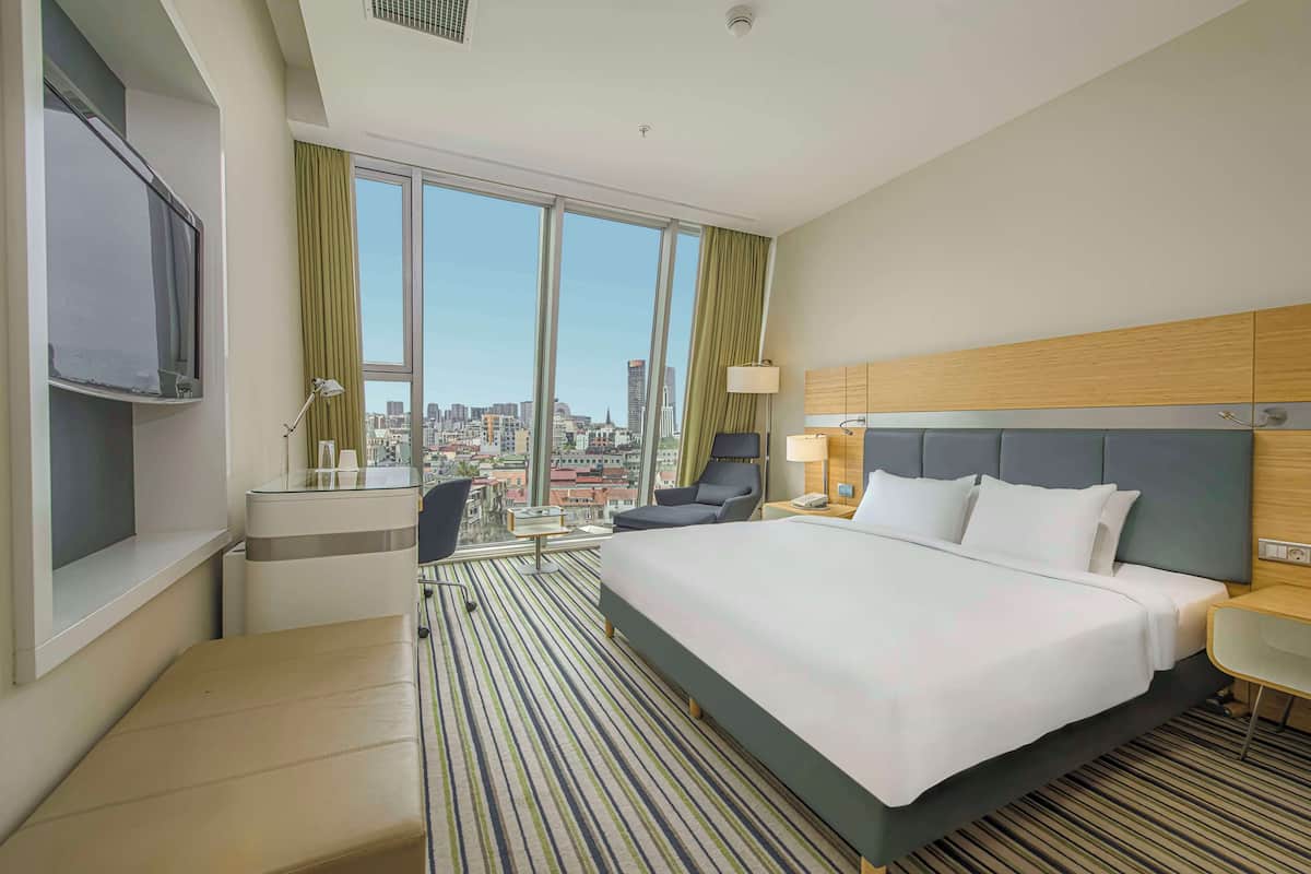 A hotel room with a large bed, a desk, a chair, and a TV.