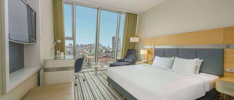 A hotel room with a large bed, a desk, a chair, and a TV.