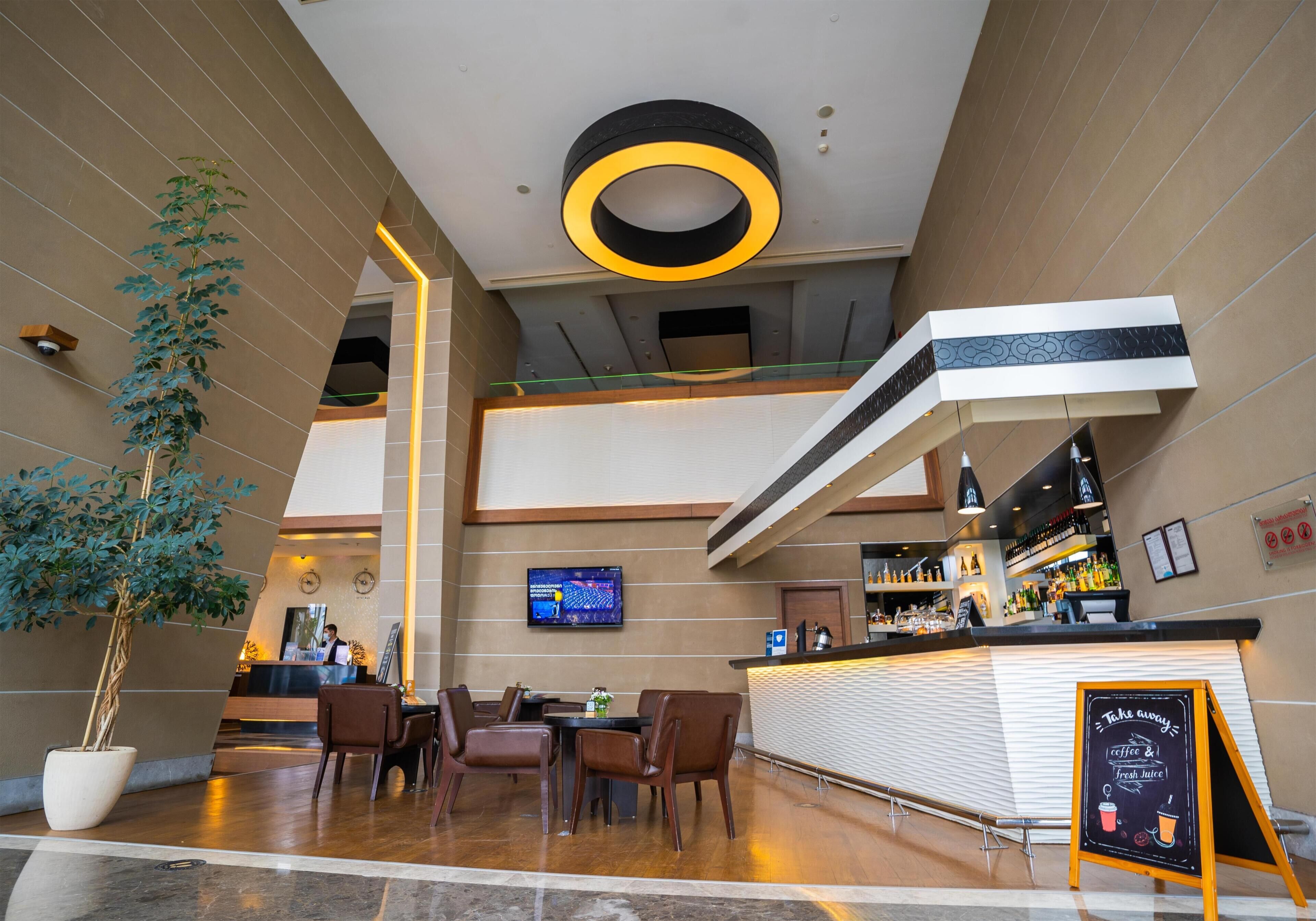 A modern hotel lobby with a reception desk, seating area, and a bar.