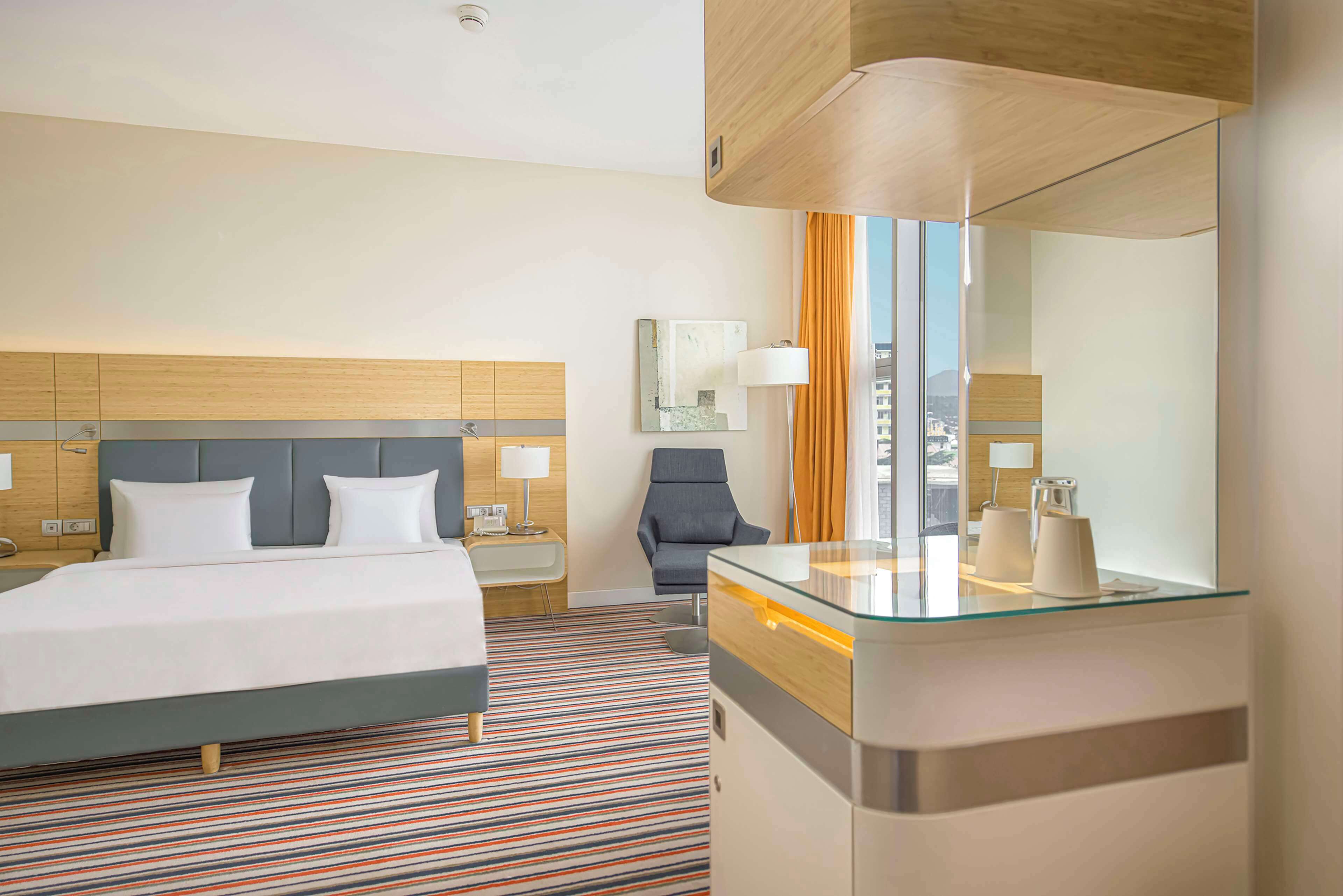 Een moderne hotelkamer met een groot bed, een glazen bureau, een stoel, een spiegel en uitzicht op de stad.