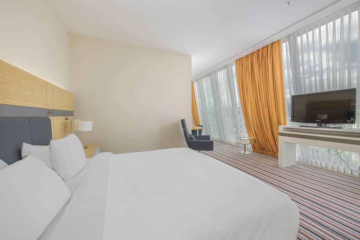 A hotel room with a large bed, a TV, a desk, and a chair.