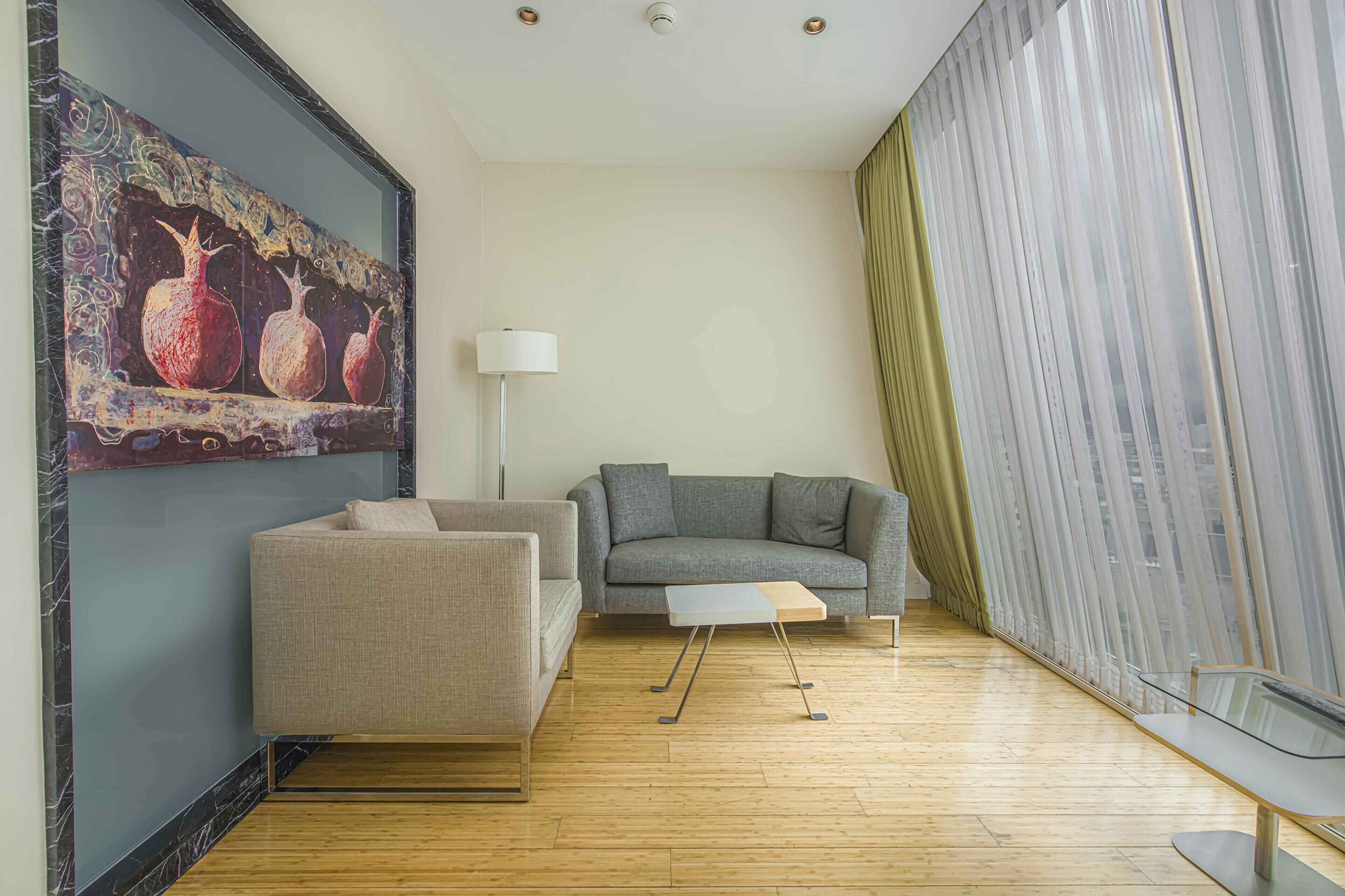 Una sala de estar moderna con un sofá gris, un sillón color beige, una mesa de centro de vidrio y un cuadro de granadas en la pared.