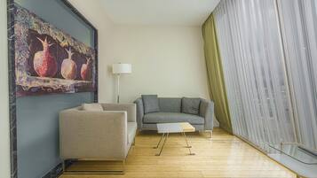 Una sala de estar moderna con un sofá gris, un sillón color beige, una mesa de centro de vidrio y un cuadro de granadas en la pared.