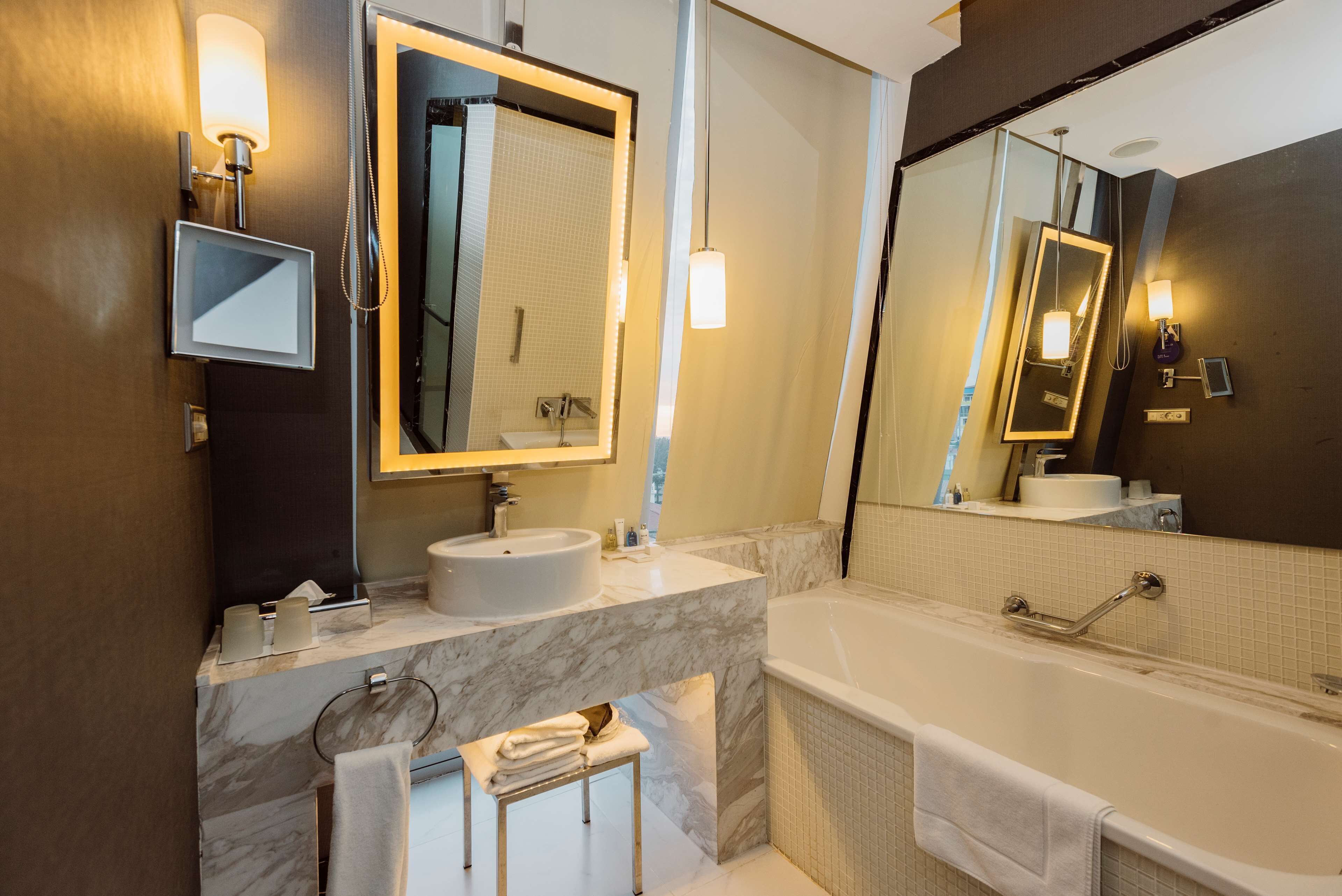 Une salle de bain moderne avec un meuble-lavabo en marbre, un grand miroir, une baignoire et un porte-serviettes.