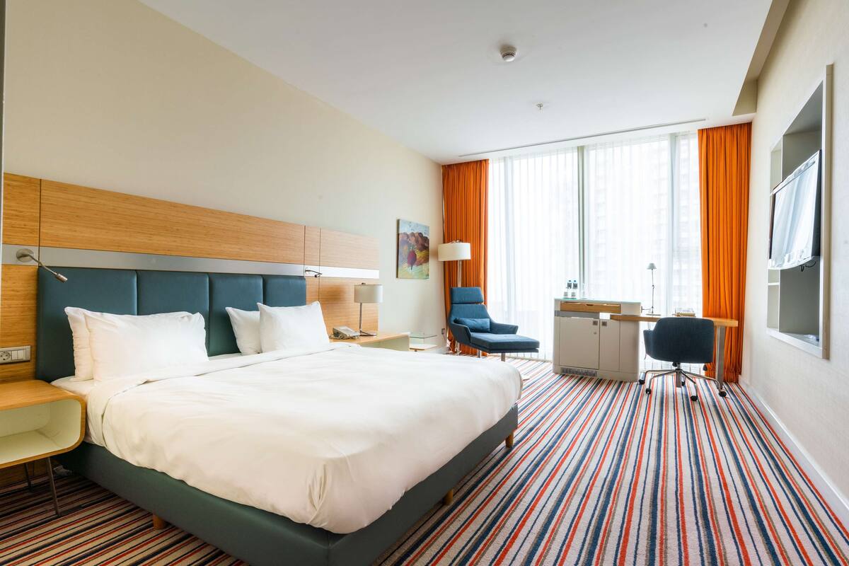 A hotel room with a large bed, a desk, a chair, and a TV.