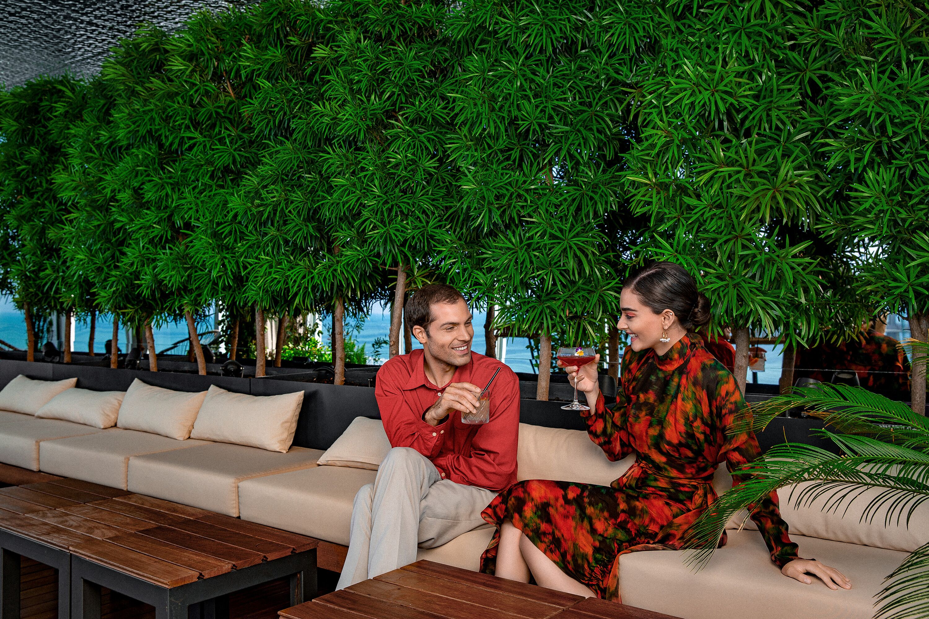 A couple seated on a sofa with a view of a tropical garden and the sea.