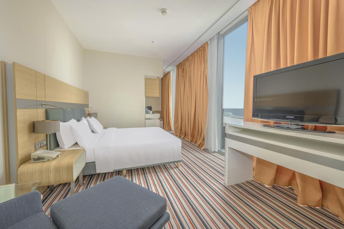 A hotel room with a bed, a desk with a television, a chair, and a window with curtains.