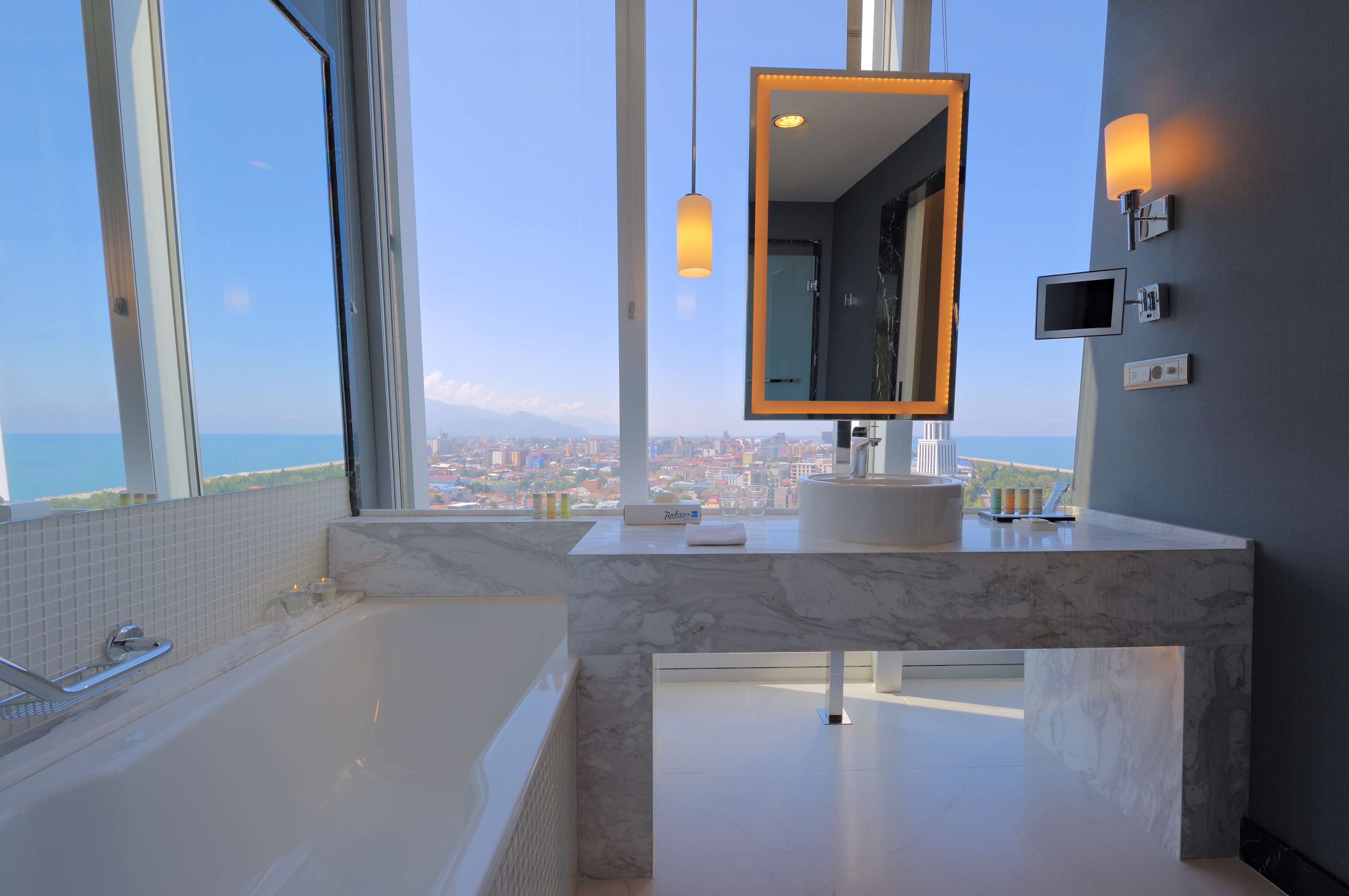 A modern bathroom with a large bathtub, a vanity with a mirror, and a view of the cityscape.