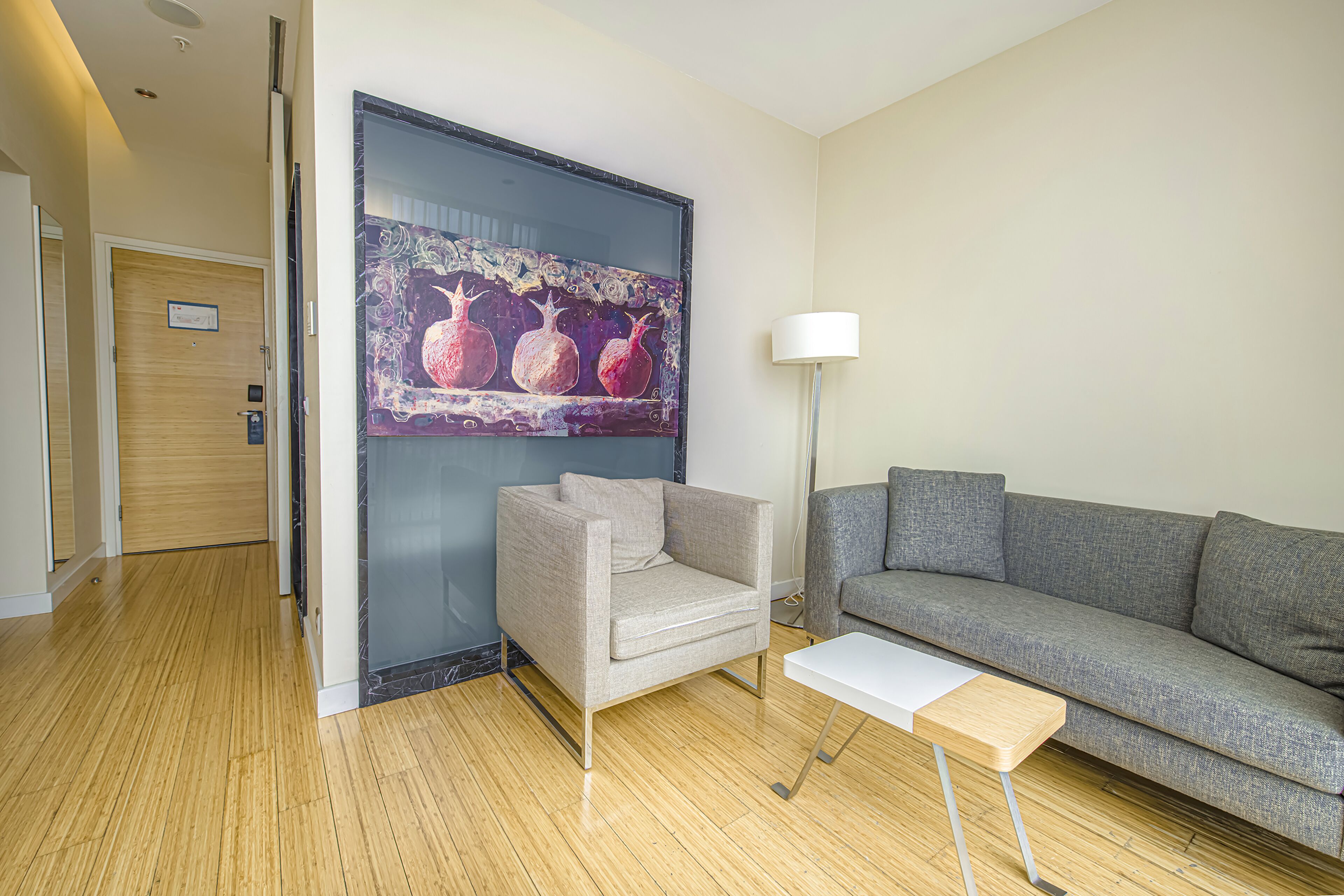 A modern room with a grey sofa, a grey armchair, a white table, and a painting of pomegranates on the wall.