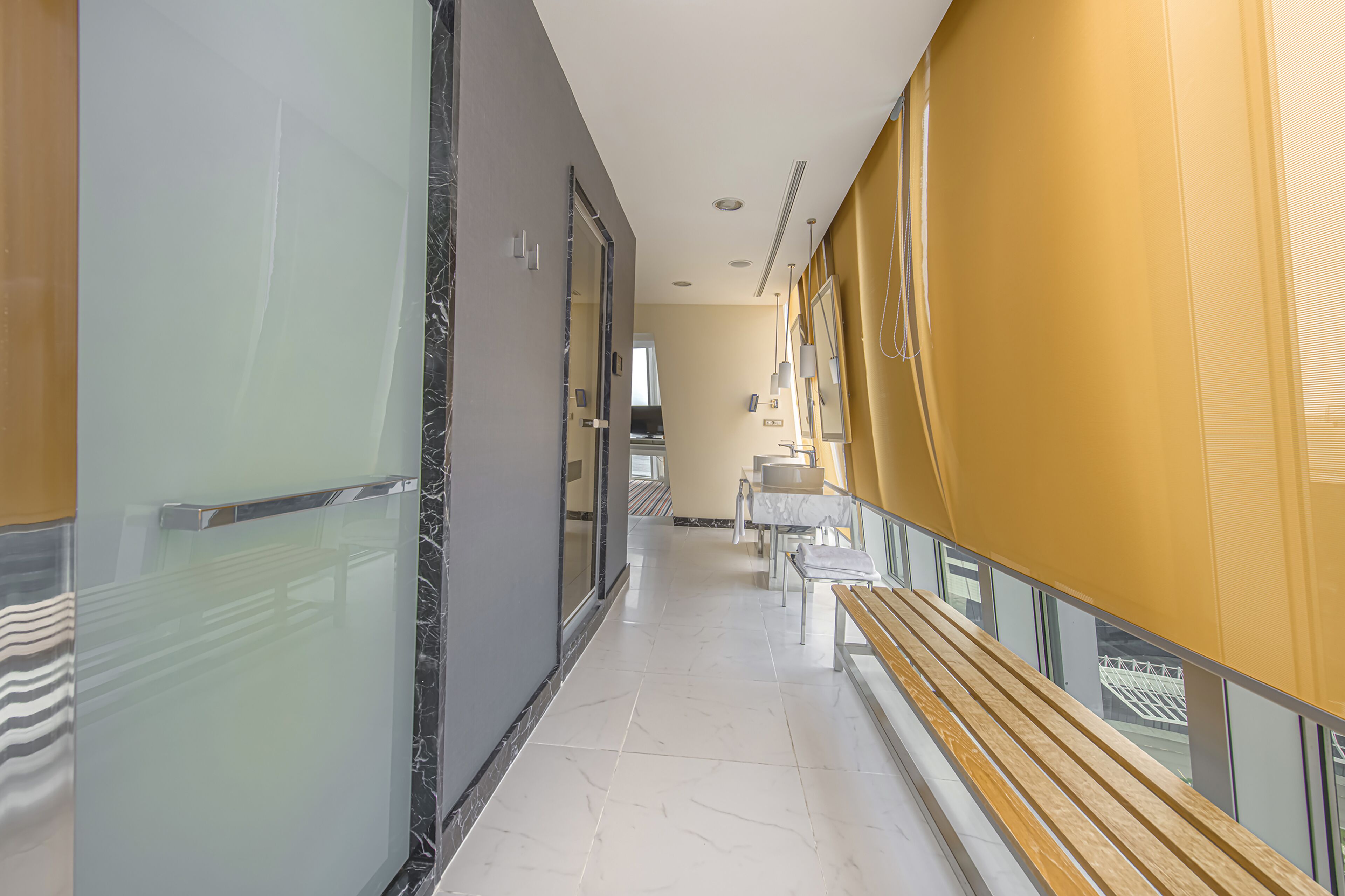 A corridor with glass walls, a marble floor, and a bench.