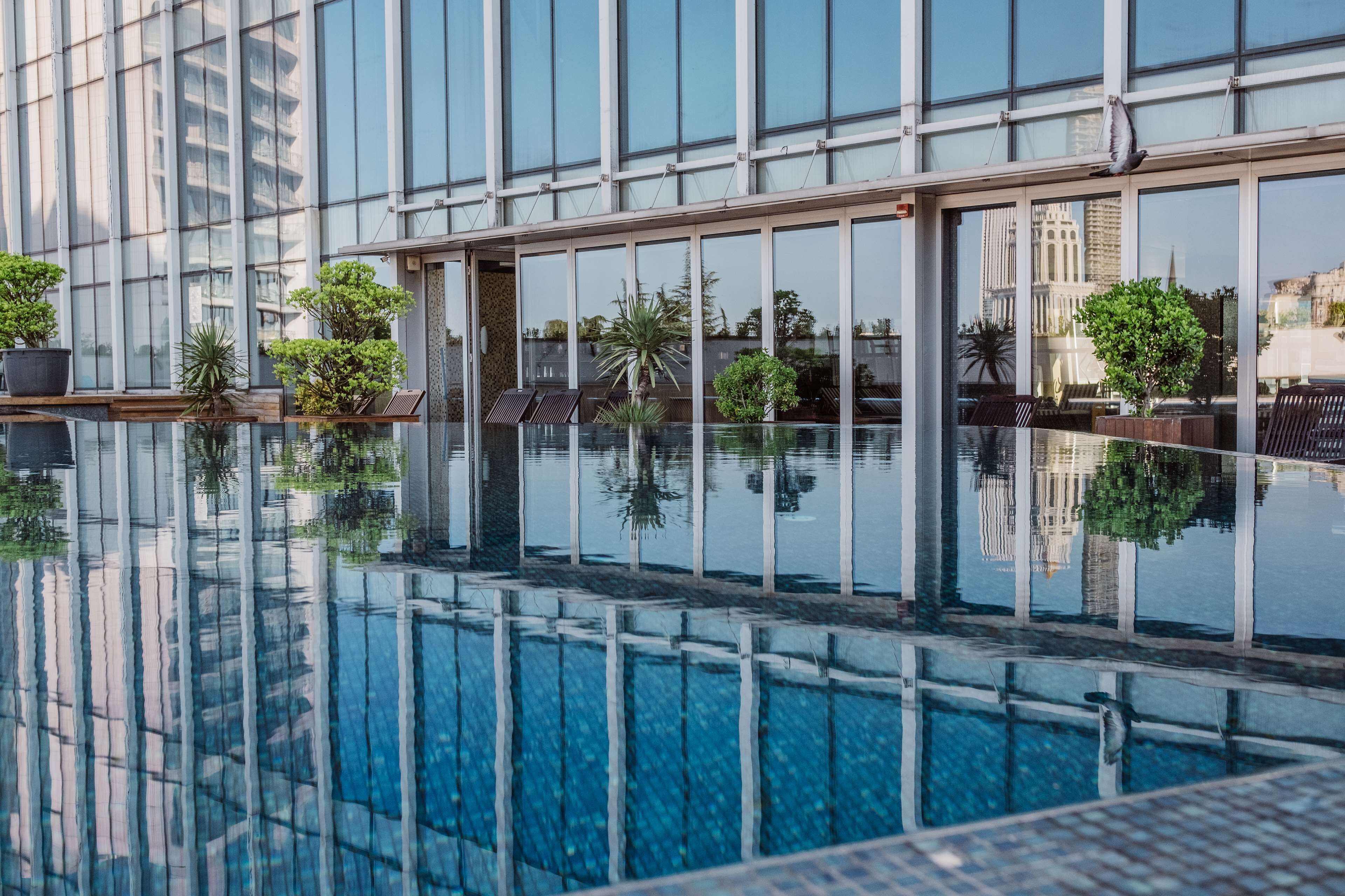 Een modern hotel met een groot binnenzwembad, glazen wanden en potplanten.