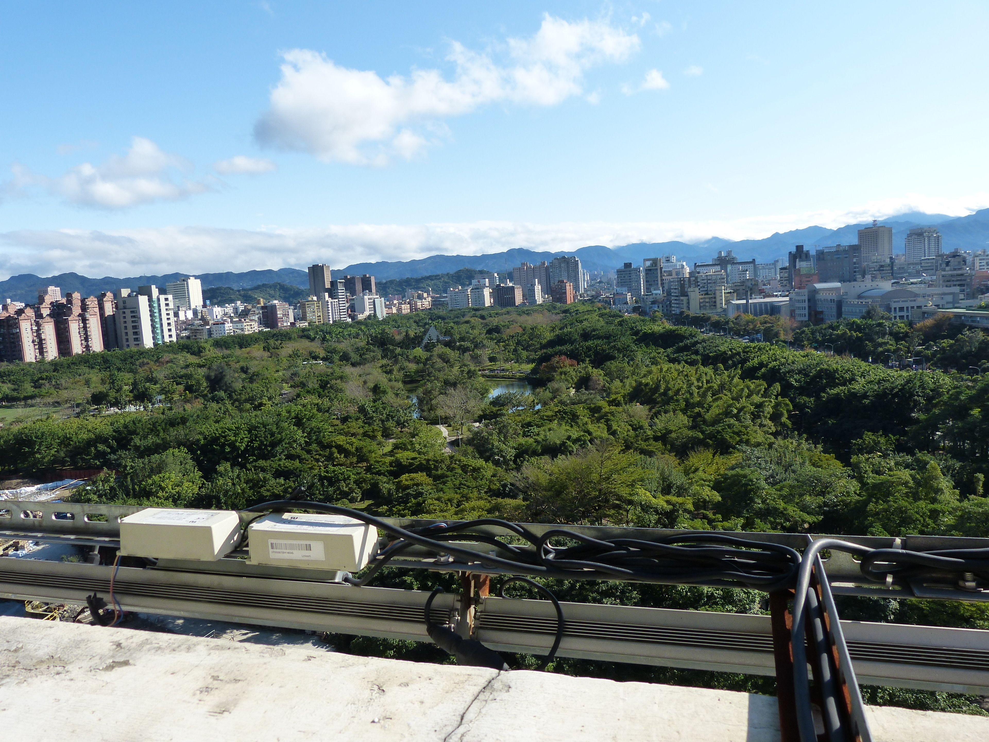 A cityscape with dense greenery and high-rise buildings in the background.