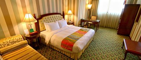Una habitación de hotel con una cama grande, dos mesitas de noche con lámparas, una silla, un escritorio y un armario.