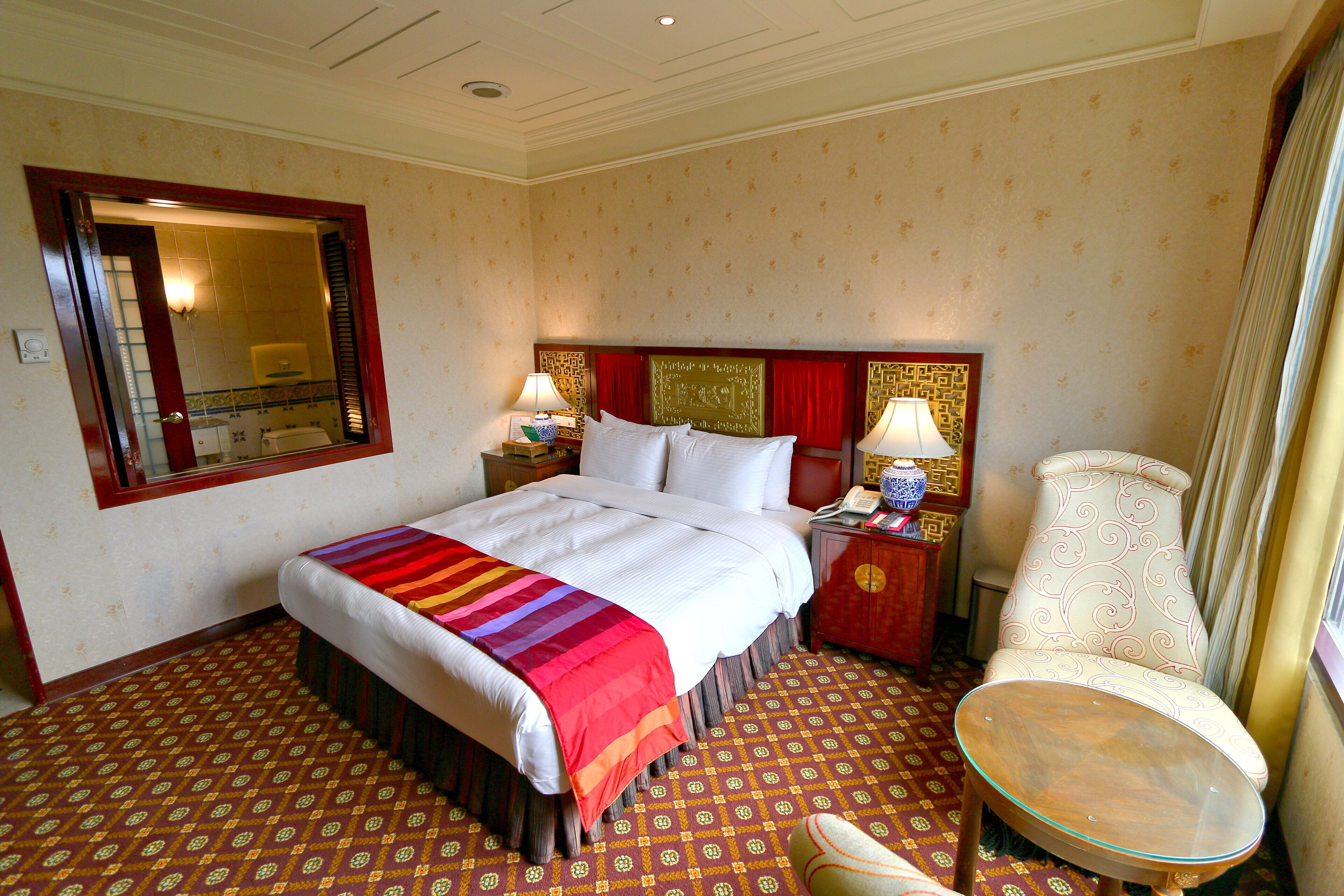 A hotel room with a bed, bedside tables, a chair, and a small table.
