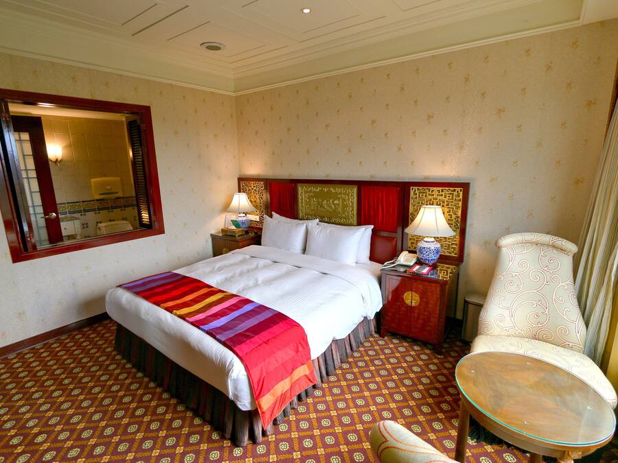 A hotel room with a bed, bedside tables, a chair, and a small table.
