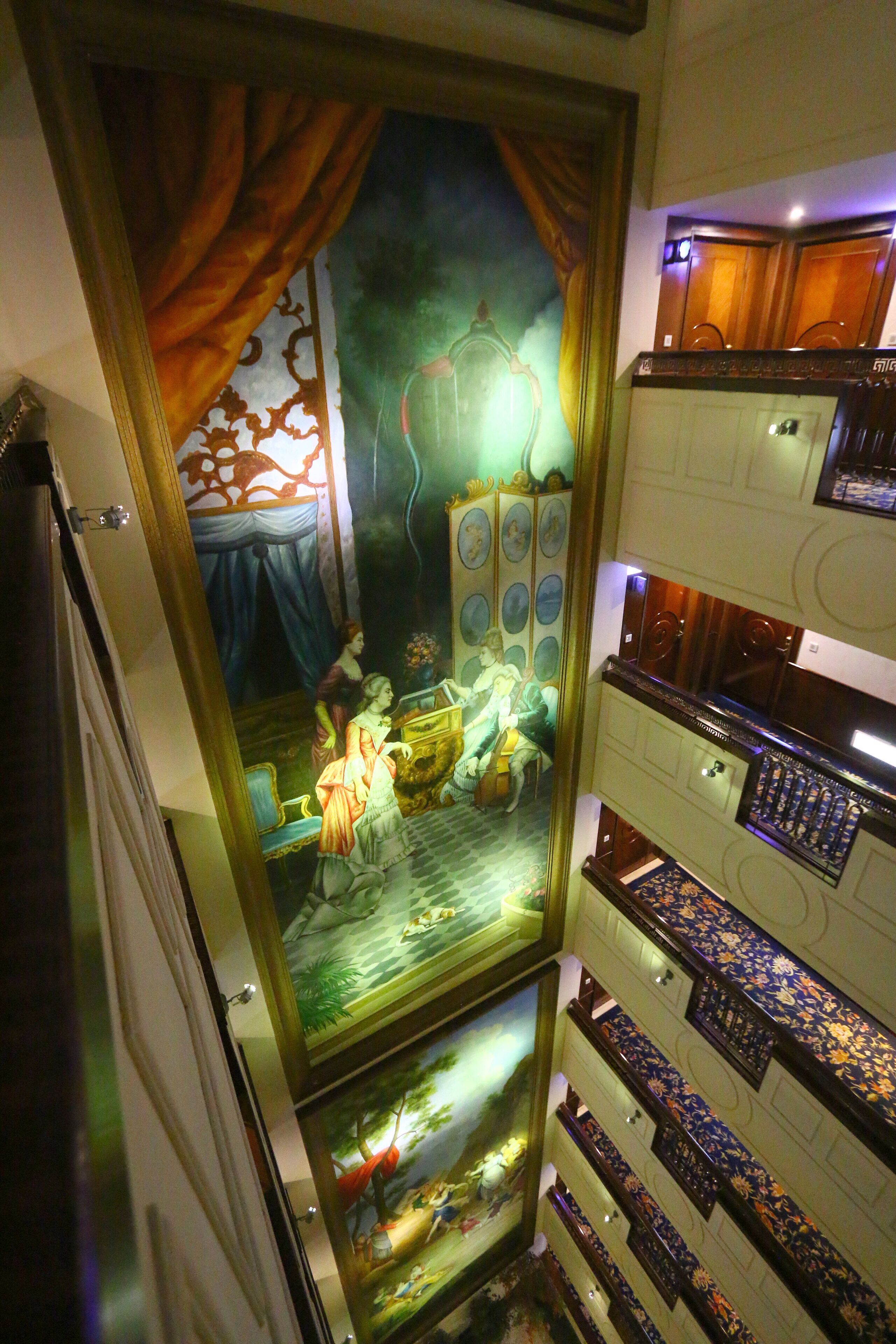 Een kamer met een grote spiegel die een schilderij van een vrouw in een groene jurk weerspiegelt. Er is een bed met een houten hoofdeinde en een nachtkastje met een lamp. De kamer heeft een houten vloer en een raam met gordijnen.