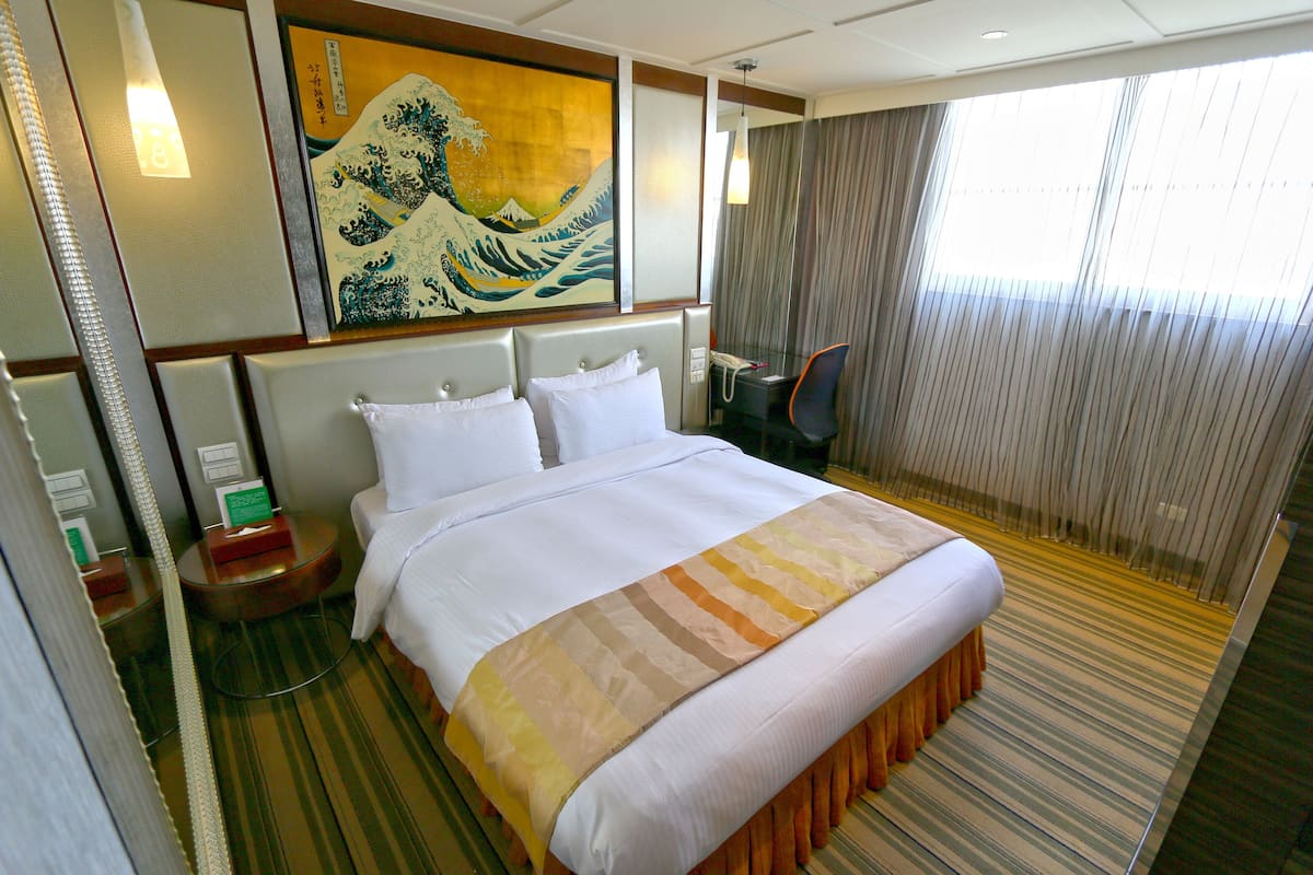 Una habitación de hotel con una cama grande, una mesita de noche, una silla y un cuadro en la pared.