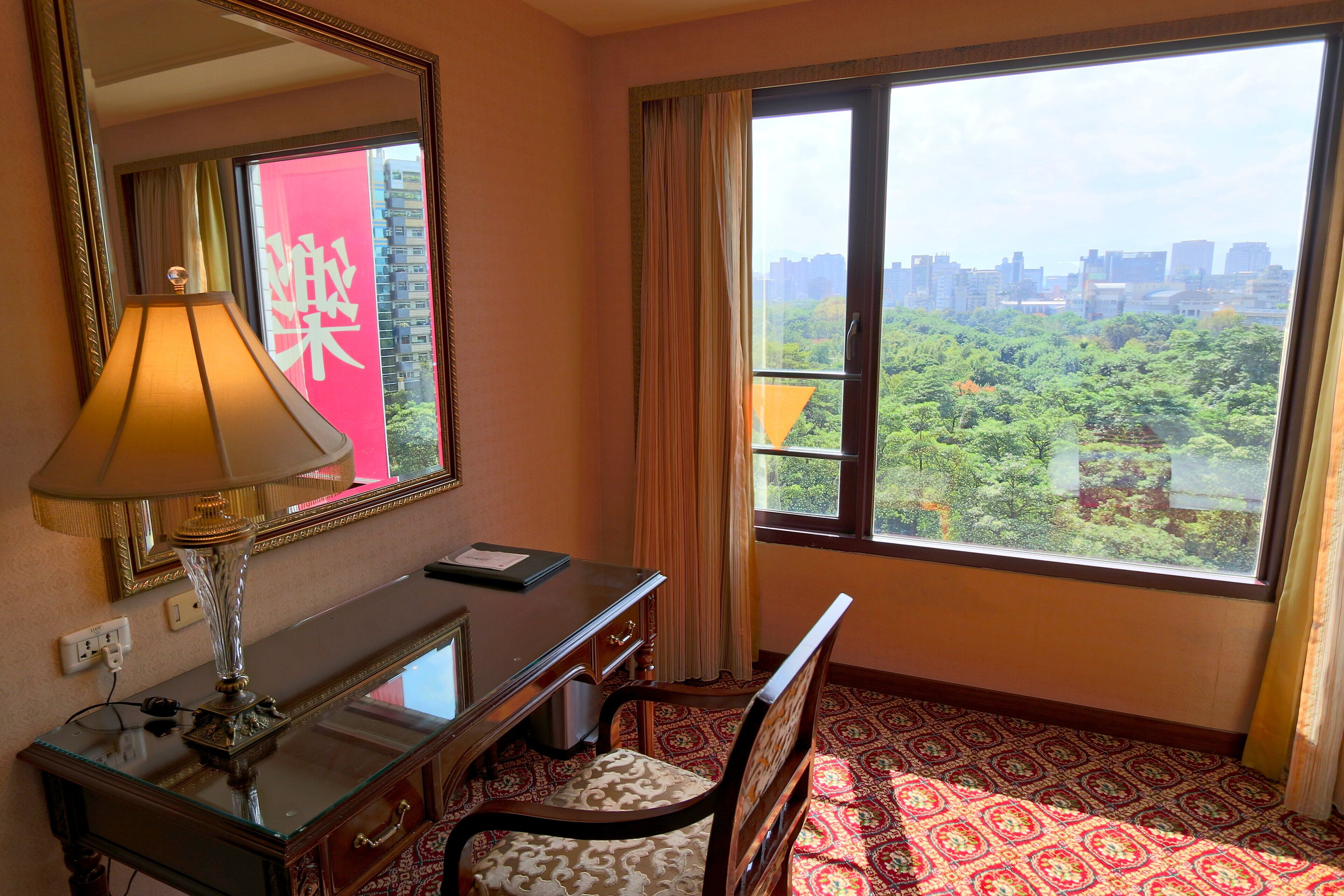 Une chambre d’hôtel équipée d’un bureau, d’une chaise et d’une grande fenêtre donnant sur le paysage urbain.