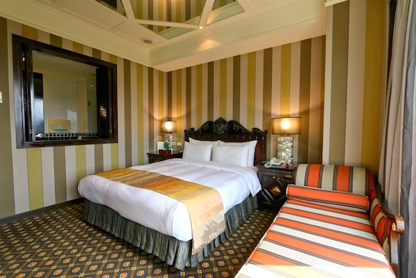 A hotel room with a large bed, a bedside table with a lamp, a chair, and a large mirror on the wall.
