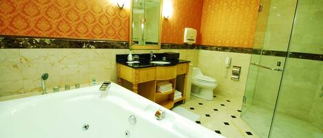 Un baño con una bañera grande, cabina de ducha con mampara de vidrio, inodoro y tocador con espejo.