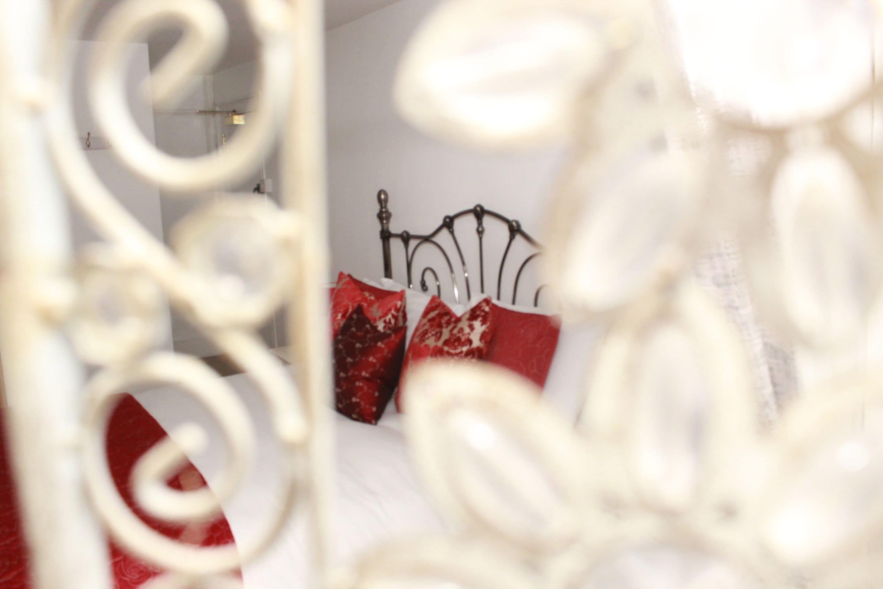 Una cama con estructura metálica y almohadas con estampado rojo y blanco.