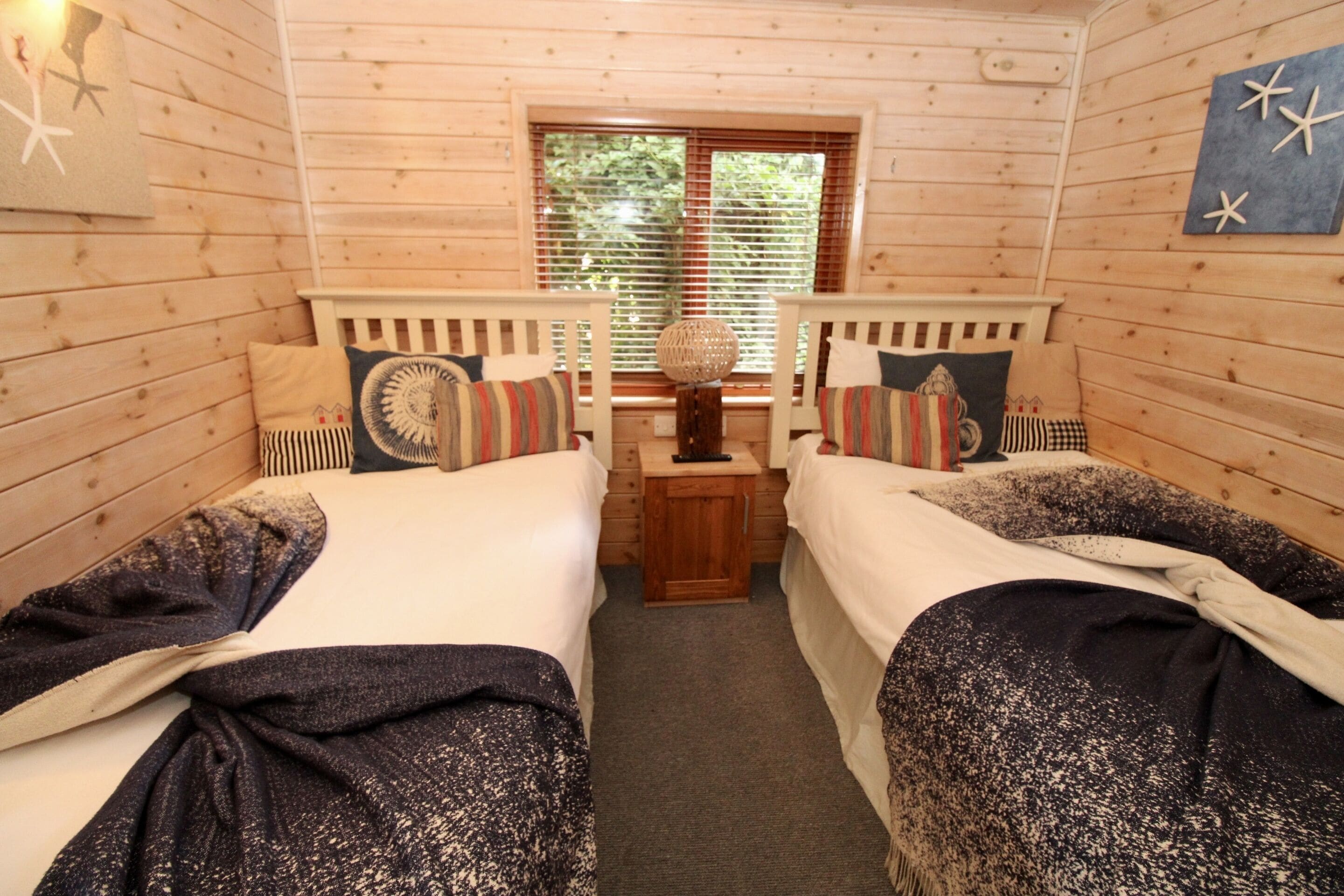 A cabin-style room with two single beds, a small wooden table, and a window with blinds.