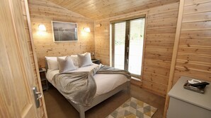 A wooden-paneled room with a bed, bedside lamps, a window with blinds, and a small desk with a tray.