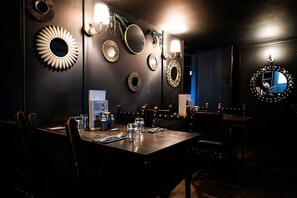 Une salle à manger à la lumière tamisée, avec plusieurs tables, des chaises et des miroirs fixés aux murs.