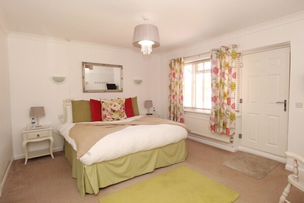 A bedroom with a bed, nightstands, a mirror, a window with floral curtains, and a door.