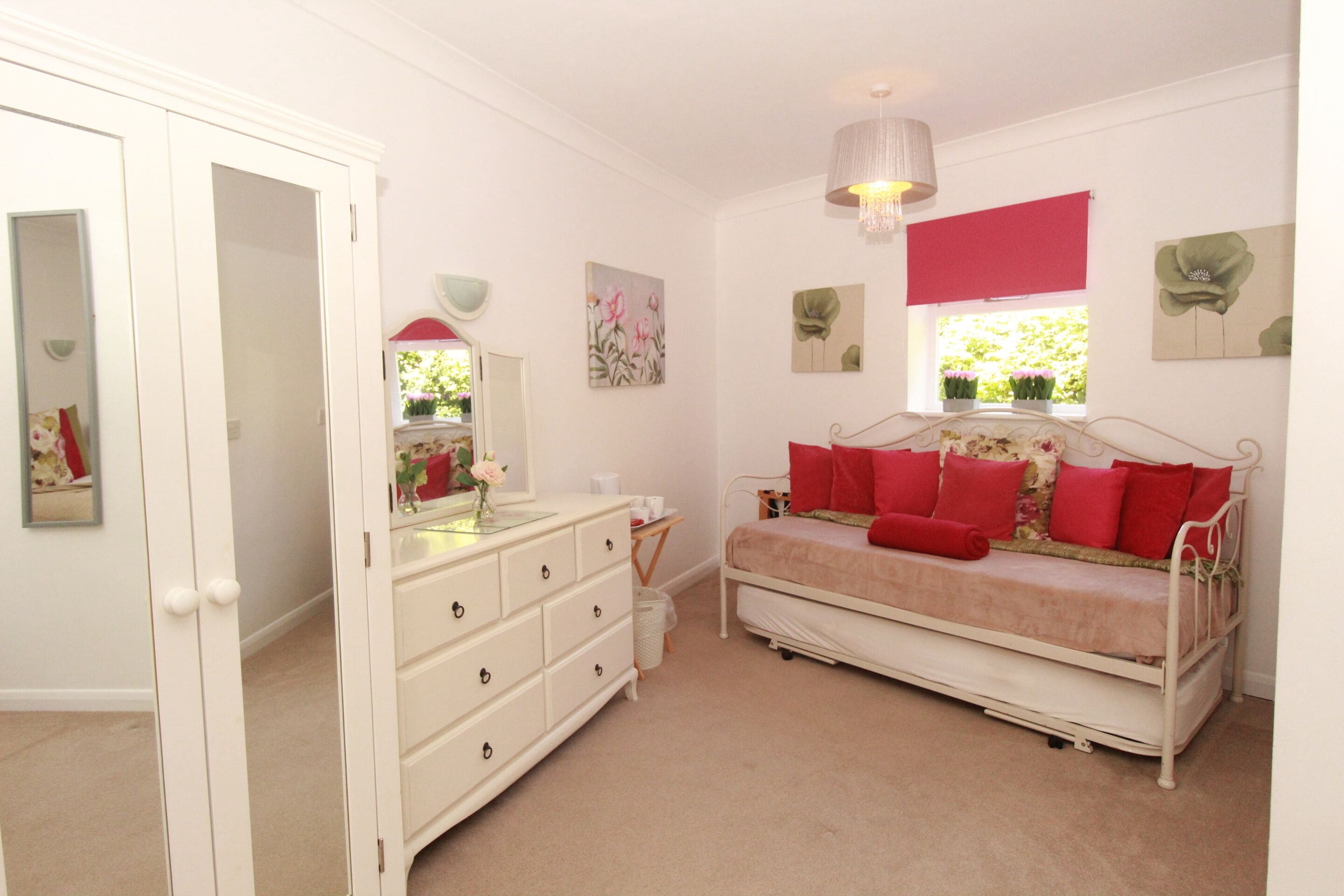 A bedroom with a bed, dresser, and a window with a view of greenery.