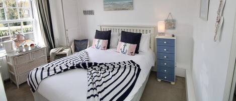 A bedroom with a bed, bedside table, dresser, and a window with curtains.