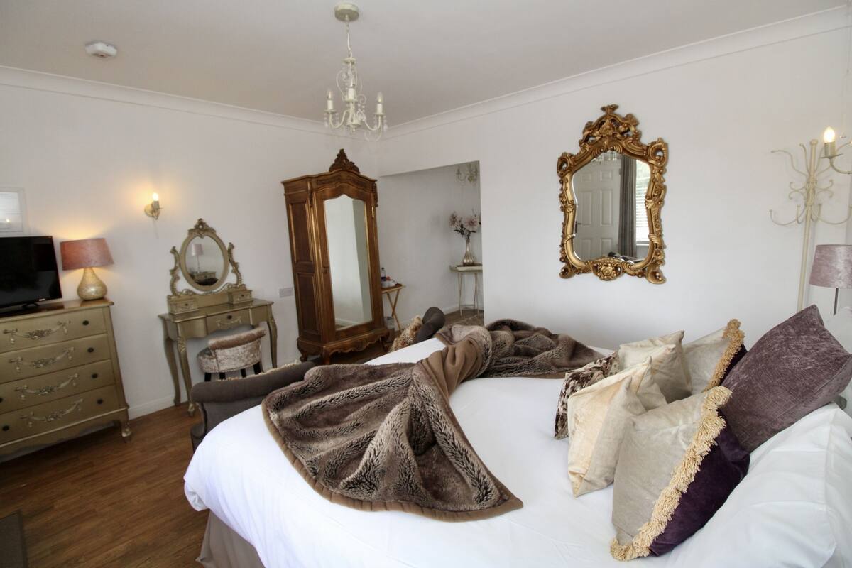 Quarto com cama, penteadeira, televisão, espelho e lustre.