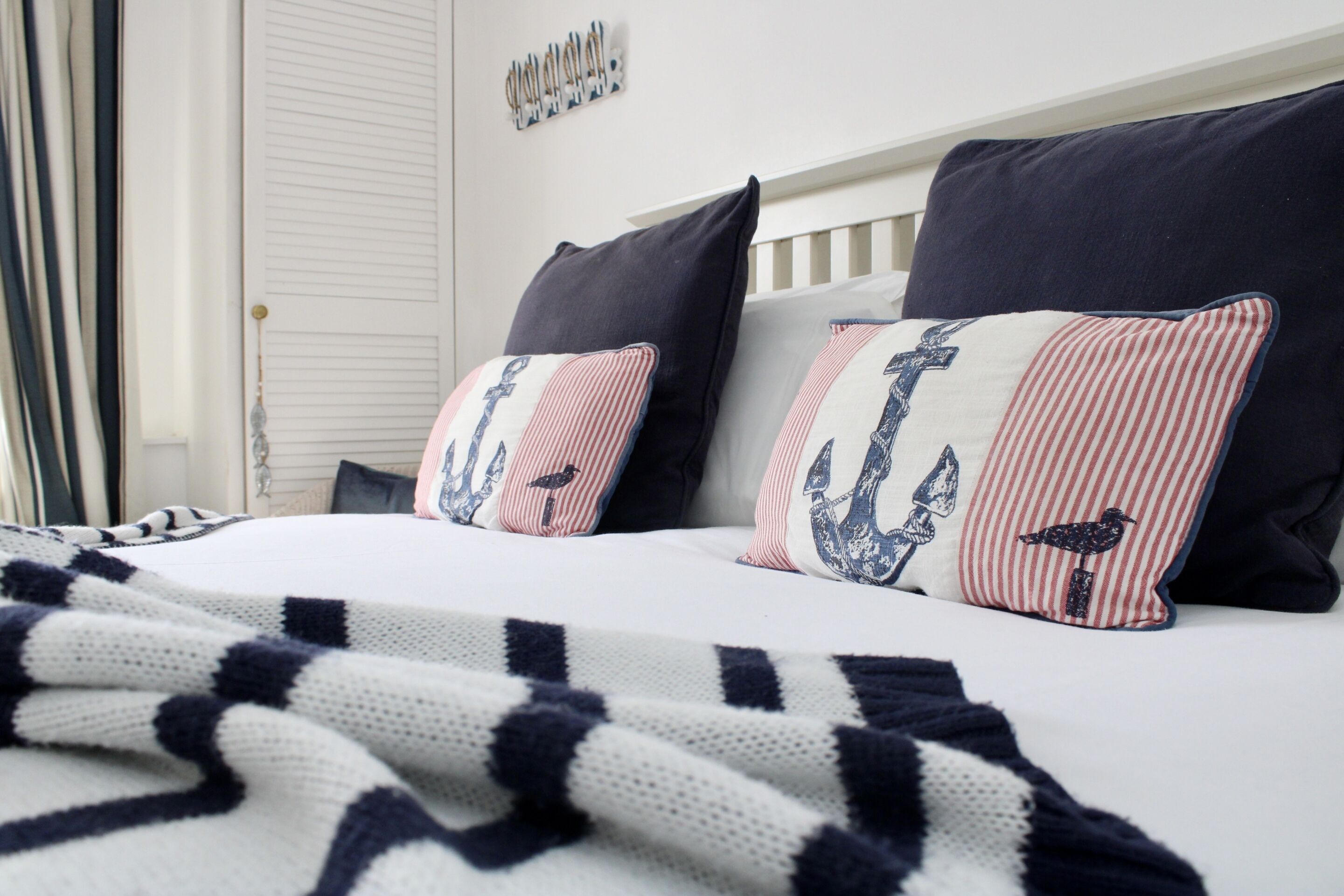 Ein Bett mit gestreifter Bettwäsche, zwei Kissen mit Anker-Motiven und einer Wanddekoration im Seestil.
