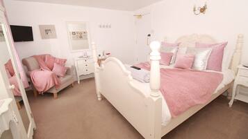 A bedroom with a white four-poster bed, a vanity with a mirror, and a dresser.