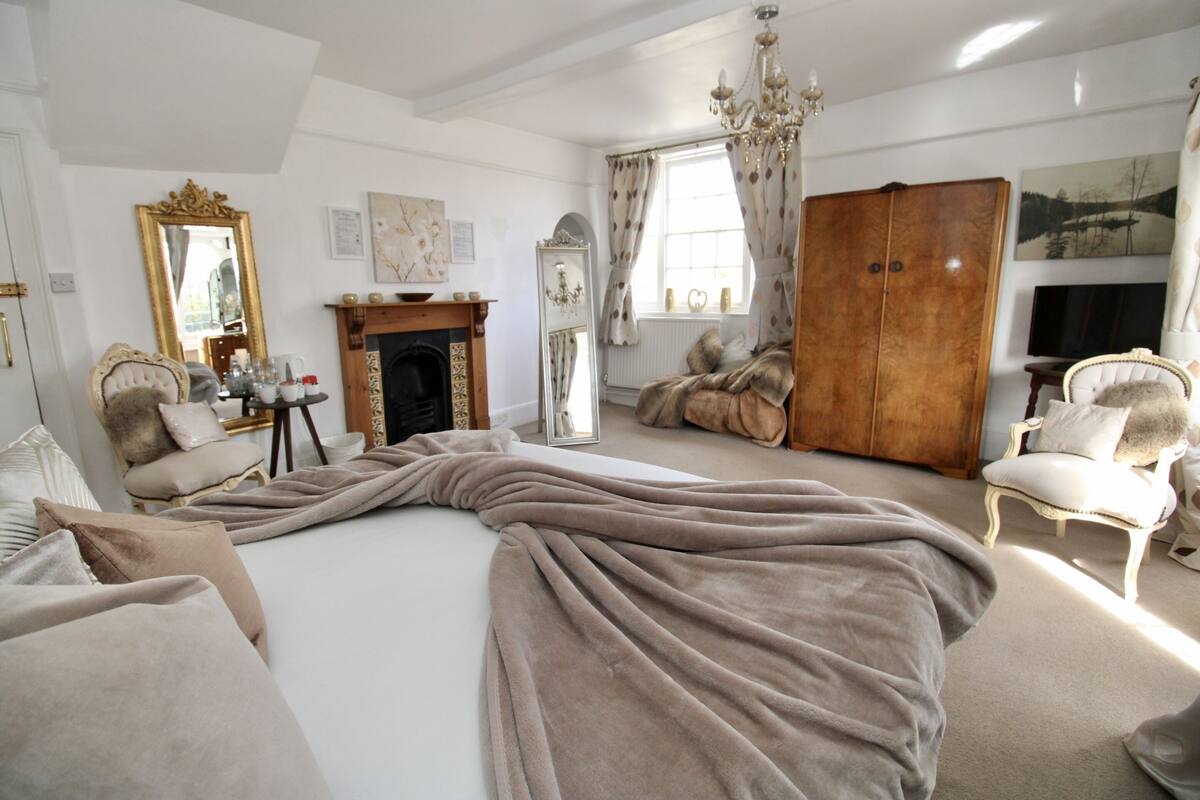 Quarto com cama grande, lareira, guarda-roupa e lustre.