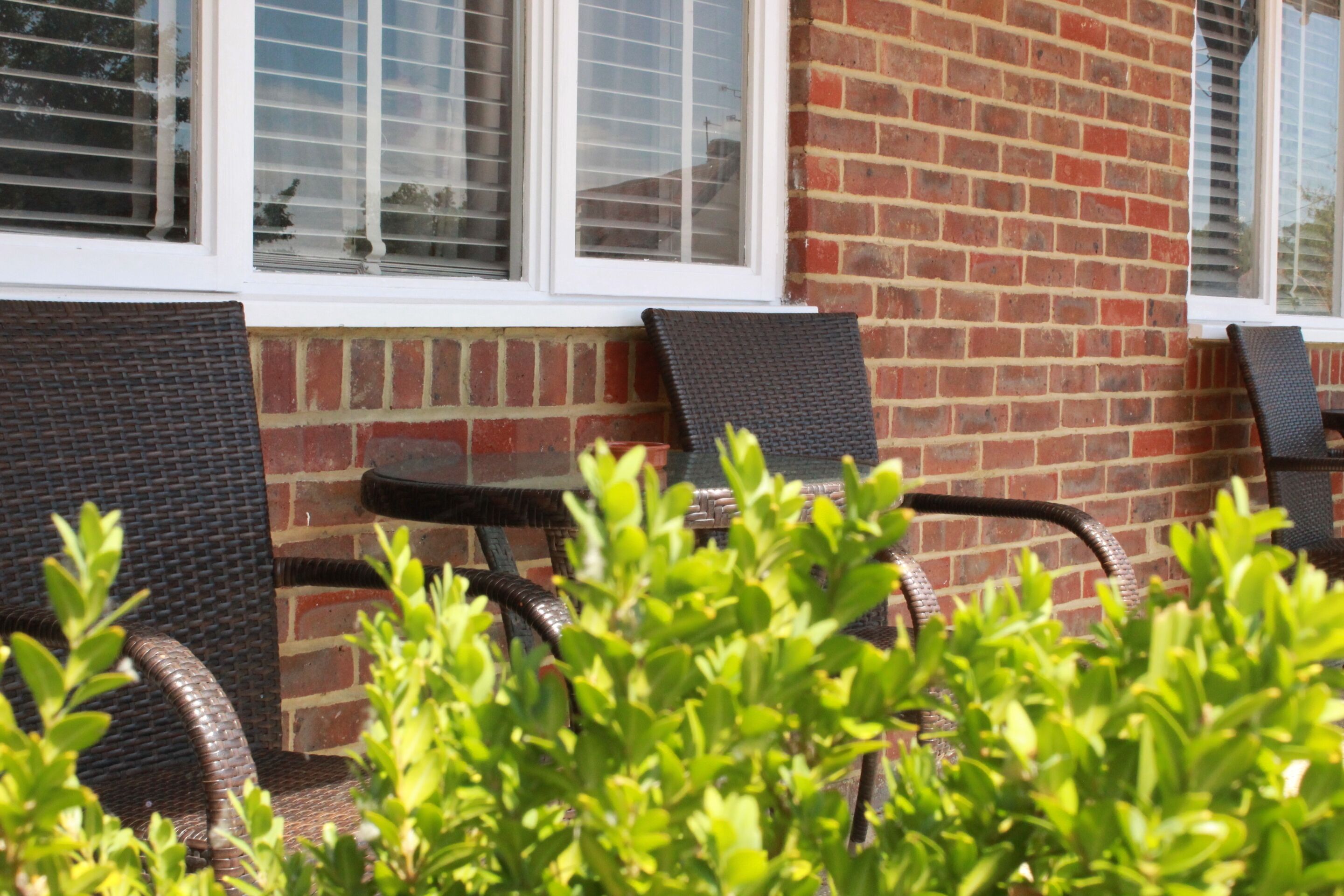 A brick building with two outdoor wicker chairs and a small table, likely a patio or garden area.