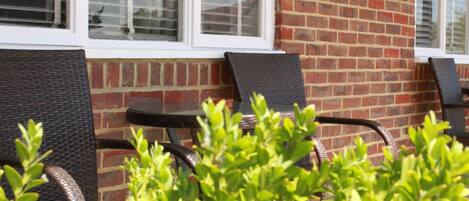 A brick building with two outdoor wicker chairs and a small table, likely a patio or garden area.