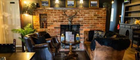 A cozy lounge area with leather sofas, a brick fireplace, and framed pictures on the wall.