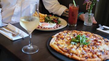 A dining table with a pizza, a salad, a Bloody Mary drink, and a glass of white wine.