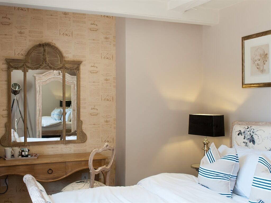 A bedroom with a large mirror, a bedside table with a lamp, and a bed with striped pillows.