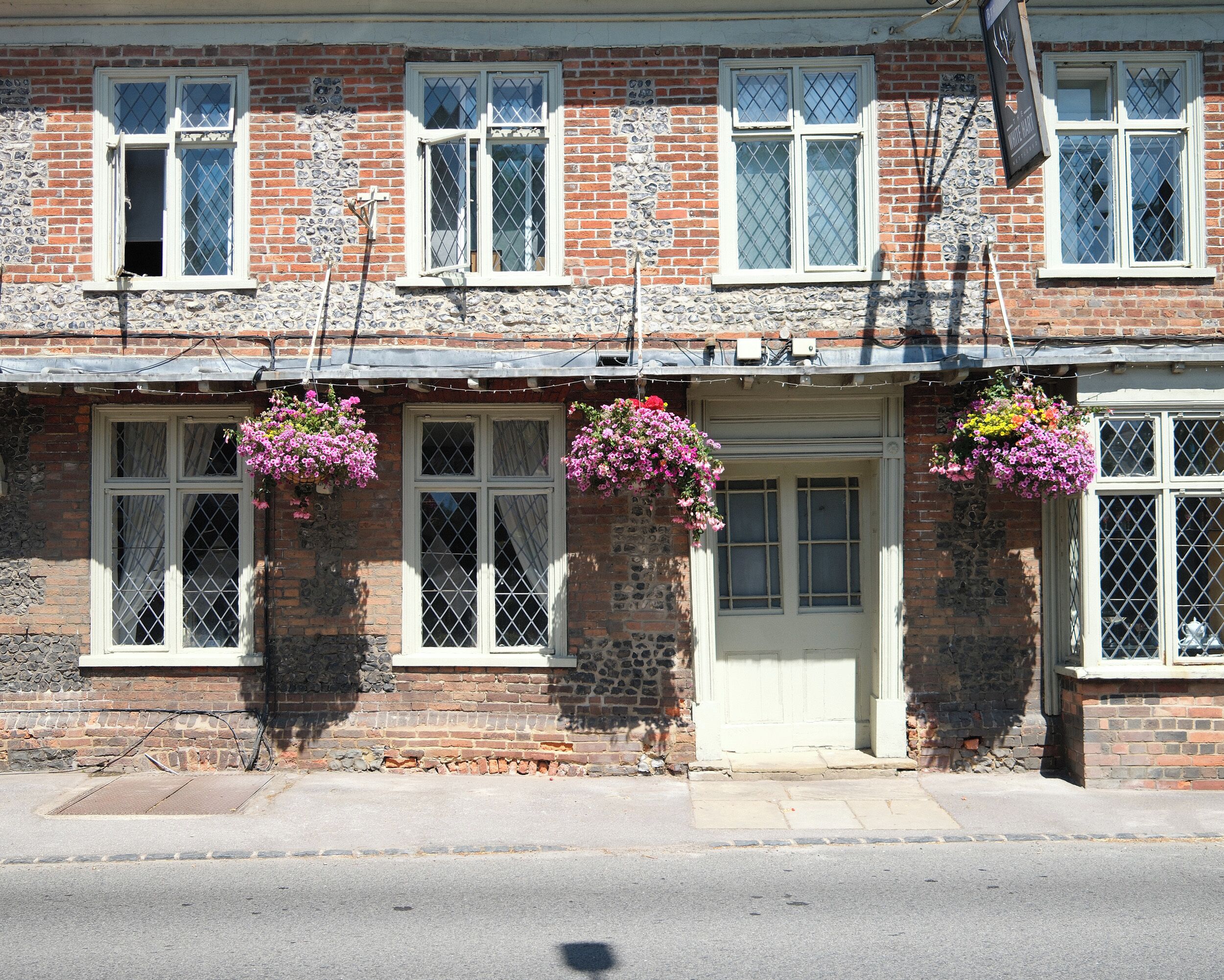 A two-story building with a brick facade, white-framed windows, and hanging flower baskets.